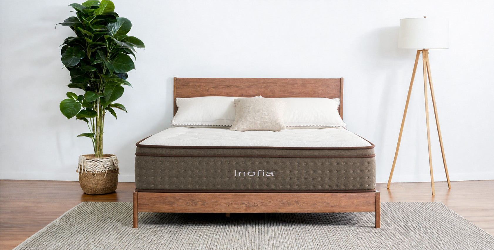 Bed with 'Inofia' mattress in a room with a plant and lamp.