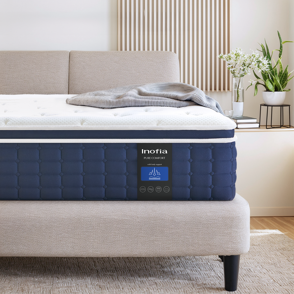 The image shows a double-sized Inofia memory foam sprung mattress, primarily in a white color, presented on a bed frame in a home setting. The mattress appears plush and is branded with the Inofia logo on a blue label.